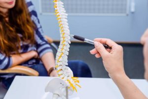 Person resting comfortably on a bed, with a spine model visible on a nearby nightstand.